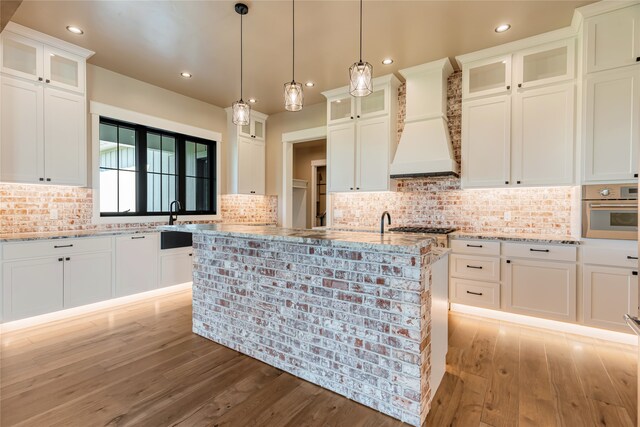 kitchen with light hardwood / wood-style floors, light stone counters, custom exhaust hood, and oven