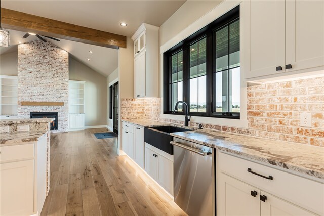 kitchen with a fireplace, light hardwood / wood-style flooring, stainless steel dishwasher, lofted ceiling with beams, and white cabinets