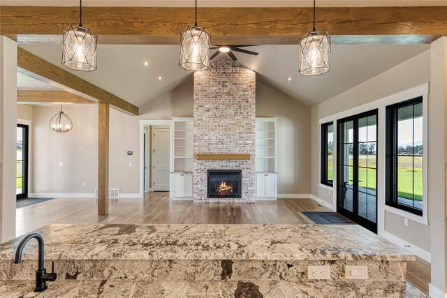 unfurnished living room featuring a stone fireplace, plenty of natural light, beamed ceiling, and light hardwood / wood-style floors