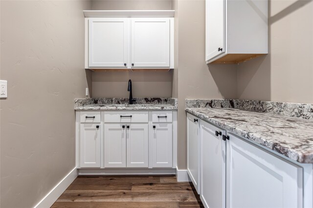 interior space with light stone counters, sink, hardwood / wood-style floors, and white cabinetry