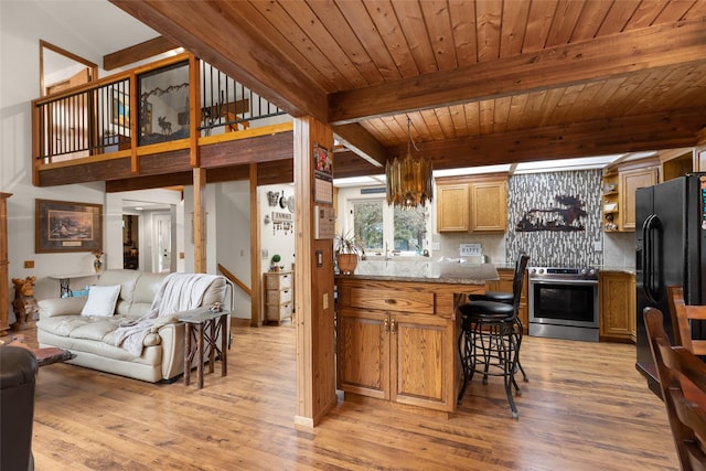 kitchen with a breakfast bar area, stainless steel range, light stone countertops, black fridge, and light wood-type flooring