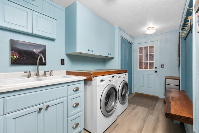 laundry room with washing machine and clothes dryer, sink, cabinets, a textured ceiling, and light wood-type flooring