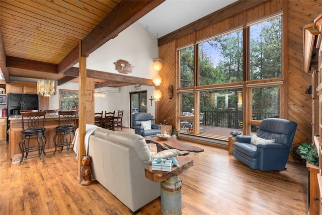 living room featuring a towering ceiling, wooden walls, beamed ceiling, a wall mounted AC, and light hardwood / wood-style floors