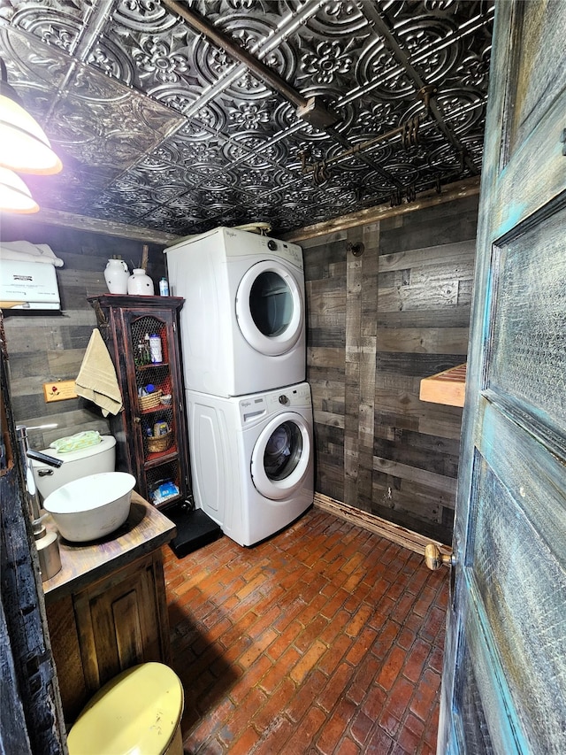 laundry area featuring wood walls and stacked washer and clothes dryer