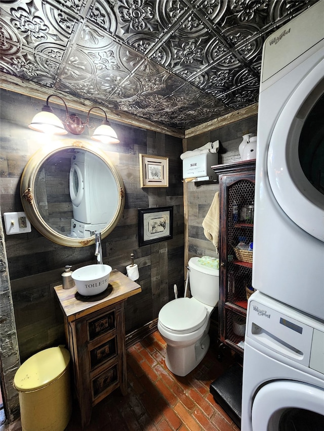 bathroom with sink, toilet, stacked washer and dryer, and wooden walls