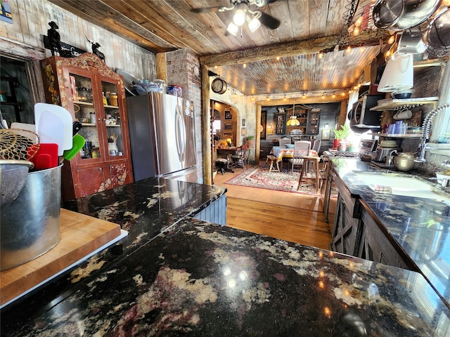 kitchen with wood-type flooring, wooden ceiling, appliances with stainless steel finishes, dark stone counters, and ceiling fan