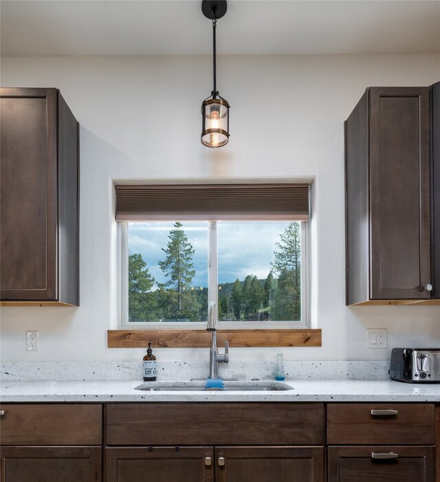 kitchen featuring sink, hanging light fixtures, dark brown cabinetry, and light stone counters