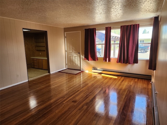 unfurnished room featuring wood walls, a baseboard heating unit, wood-type flooring, and a textured ceiling