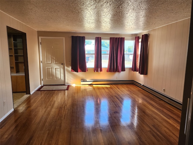 spare room with wood walls, a baseboard heating unit, wood-type flooring, and a textured ceiling