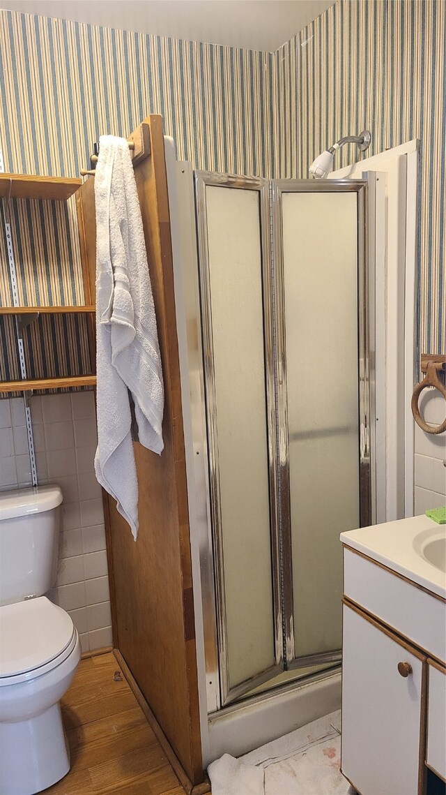 bathroom with walk in shower, vanity, wood-type flooring, tile walls, and toilet