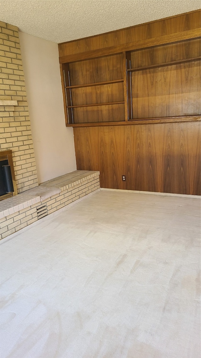 unfurnished living room featuring wooden walls, light colored carpet, and a textured ceiling