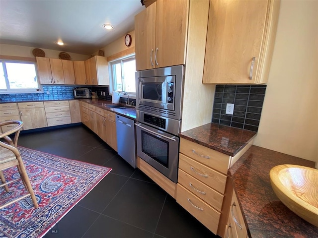 kitchen with appliances with stainless steel finishes, tasteful backsplash, light brown cabinetry, sink, and dark tile floors