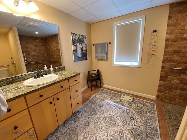 bathroom with vanity, brick wall, a paneled ceiling, and tile flooring