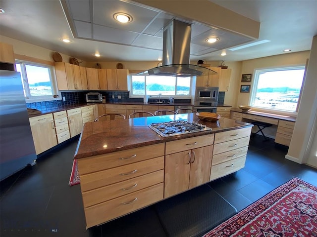 kitchen with light brown cabinetry, appliances with stainless steel finishes, island exhaust hood, tasteful backsplash, and dark tile flooring