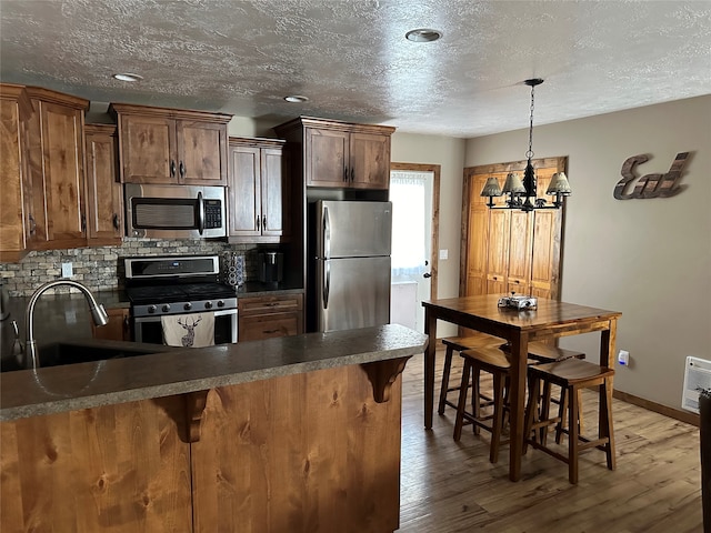 kitchen featuring stainless steel appliances, hardwood / wood-style floors, pendant lighting, sink, and tasteful backsplash