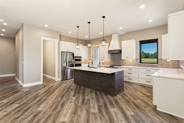 kitchen featuring premium range hood, an island with sink, dark wood-type flooring, white cabinetry, and stainless steel appliances