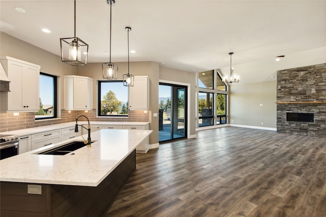 kitchen with light stone countertops, a center island with sink, hanging light fixtures, and sink