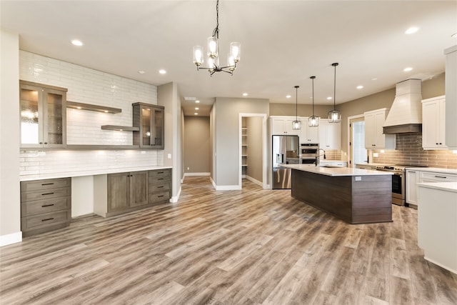 kitchen with hardwood / wood-style flooring, an island with sink, hanging light fixtures, custom exhaust hood, and stainless steel appliances