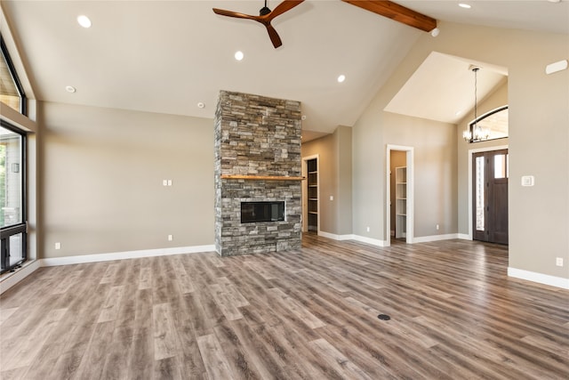 unfurnished living room with high vaulted ceiling, ceiling fan with notable chandelier, a fireplace, beamed ceiling, and hardwood / wood-style floors