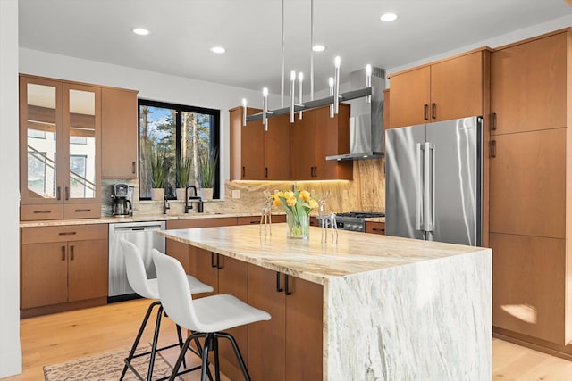 kitchen featuring light wood-type flooring, wall chimney range hood, appliances with stainless steel finishes, and a center island