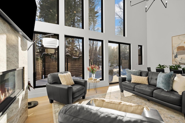 living area with a chandelier, light wood finished floors, a fireplace, and a towering ceiling