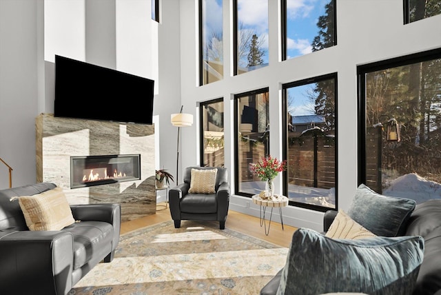 living room featuring wood finished floors, a glass covered fireplace, and a high ceiling