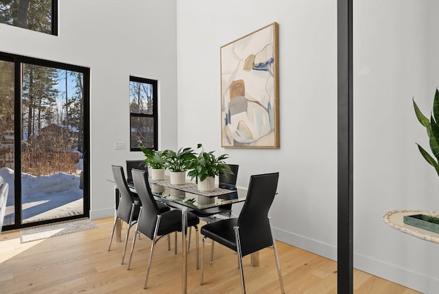 dining space featuring light wood-type flooring, a towering ceiling, and baseboards