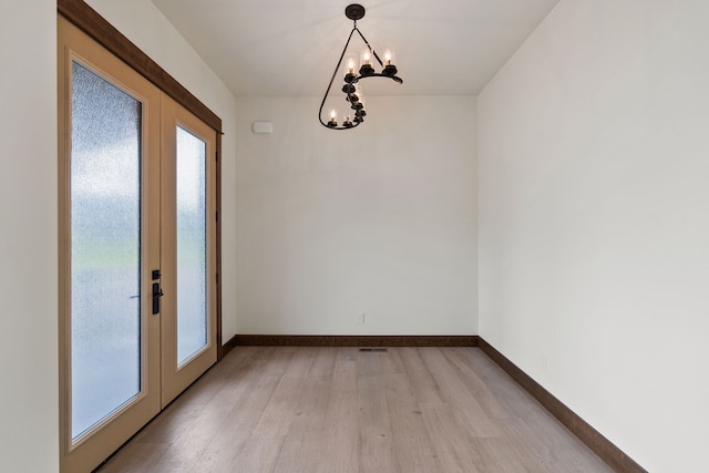 unfurnished dining area featuring a healthy amount of sunlight, light hardwood / wood-style flooring, a notable chandelier, and french doors