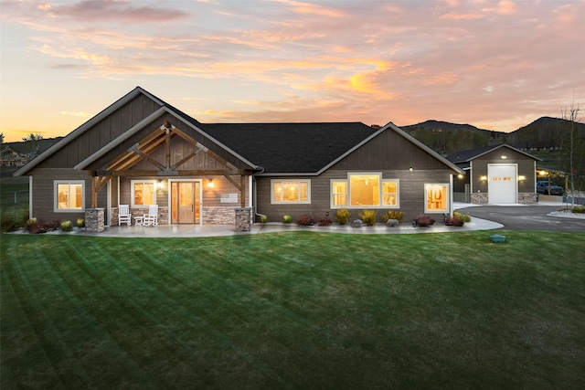 back house at dusk with a garage and a lawn