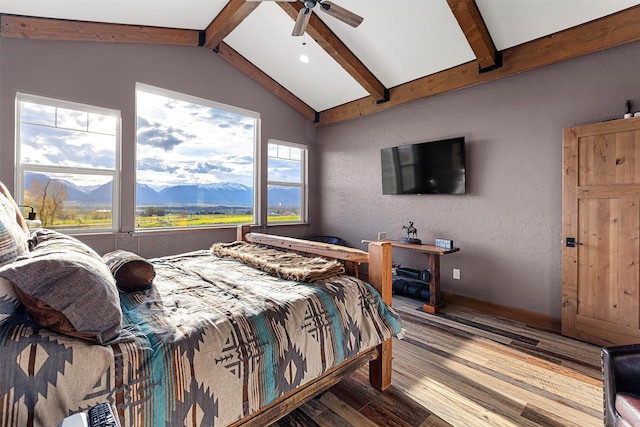 bedroom featuring a mountain view, wood-type flooring, ceiling fan, and vaulted ceiling with beams