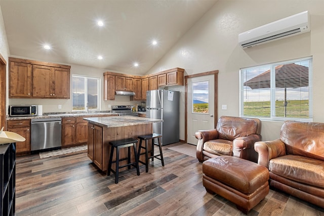 kitchen with appliances with stainless steel finishes, a wall mounted air conditioner, a kitchen island, and dark wood-type flooring