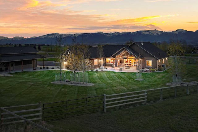 back house at dusk with a mountain view, a patio, and a lawn