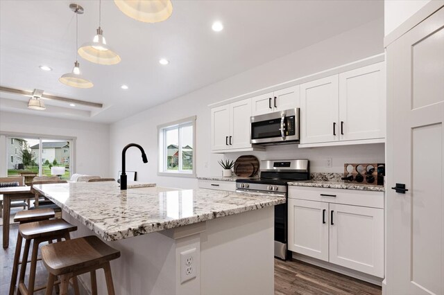 kitchen featuring a kitchen island with sink, stainless steel appliances, hanging light fixtures, dark hardwood / wood-style floors, and white cabinets