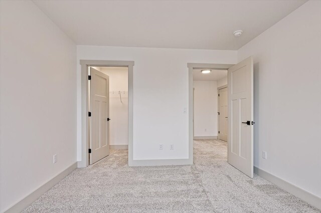 unfurnished bedroom featuring a closet, light colored carpet, and a spacious closet