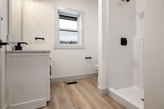 bathroom with hardwood / wood-style floors, vanity, toilet, and walk in shower