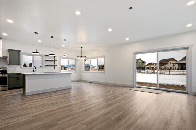 kitchen with gray cabinetry, pendant lighting, stainless steel range oven, light hardwood / wood-style floors, and a kitchen island