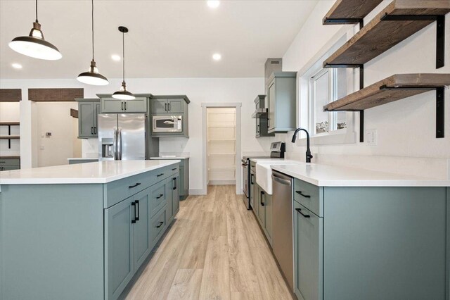 kitchen with stainless steel appliances, sink, pendant lighting, light hardwood / wood-style floors, and a kitchen island