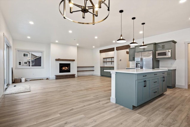 kitchen with hanging light fixtures, light hardwood / wood-style flooring, stainless steel refrigerator with ice dispenser, an island with sink, and white microwave