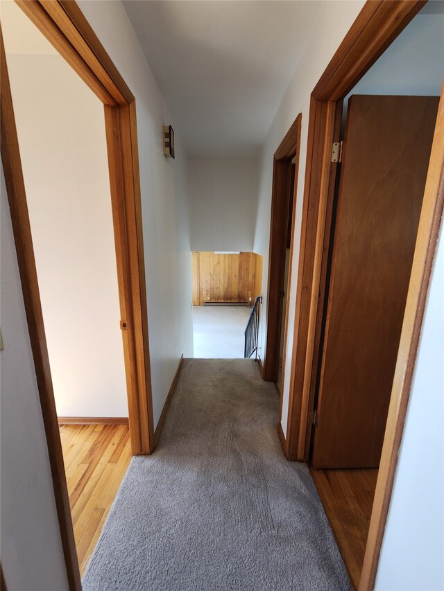 hall featuring carpet floors, wood finished floors, an upstairs landing, and baseboards