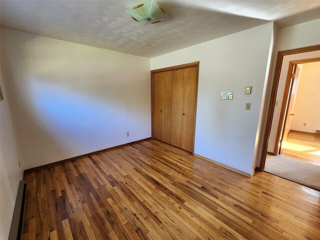 unfurnished bedroom with a closet, light wood-type flooring, a baseboard radiator, and baseboards