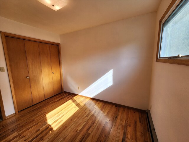 unfurnished bedroom featuring light wood-style floors, a baseboard radiator, and baseboards