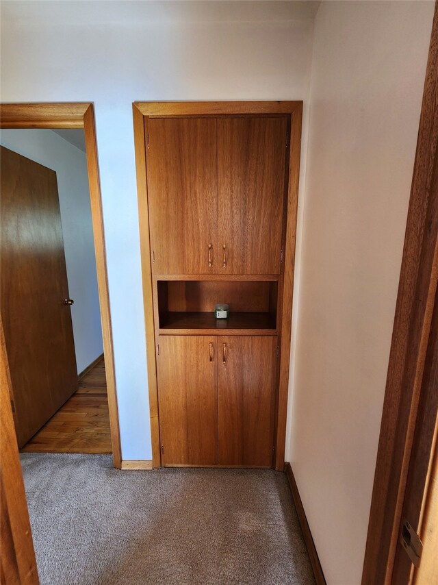 hallway featuring baseboards and dark carpet