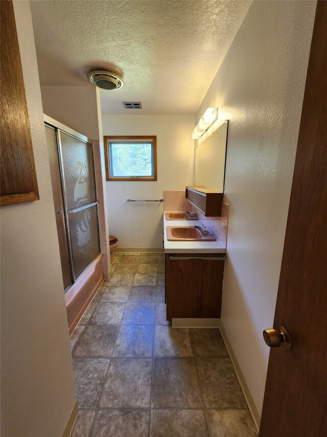 full bathroom featuring toilet, shower / bath combination with glass door, visible vents, baseboards, and double vanity