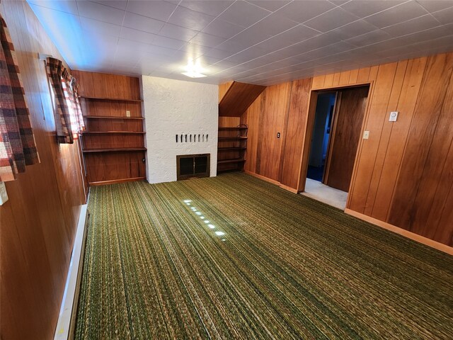 unfurnished living room with a large fireplace, baseboards, carpet floors, wood walls, and built in shelves