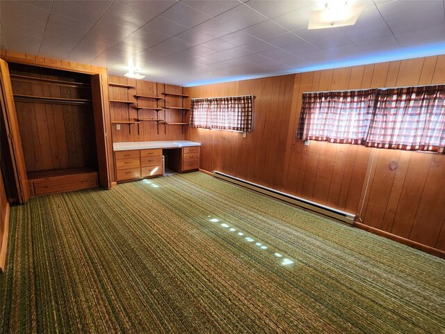 unfurnished office featuring a wealth of natural light, dark carpet, baseboard heating, built in study area, and wood walls