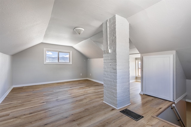 bonus room featuring light hardwood / wood-style floors, lofted ceiling, and a textured ceiling