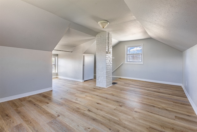 bonus room featuring decorative columns, vaulted ceiling, a textured ceiling, and light hardwood / wood-style floors