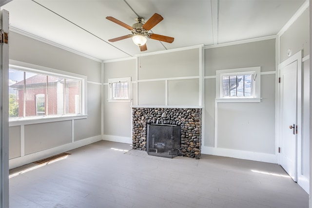 unfurnished living room featuring a stone fireplace, ornamental molding, light wood-type flooring, and ceiling fan