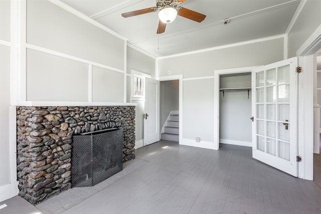 unfurnished living room with crown molding, a stone fireplace, wood-type flooring, and ceiling fan