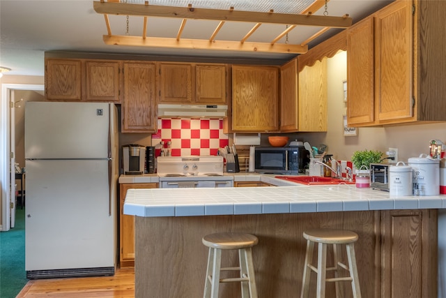 kitchen featuring a kitchen breakfast bar, white appliances, light wood-type flooring, kitchen peninsula, and tile countertops